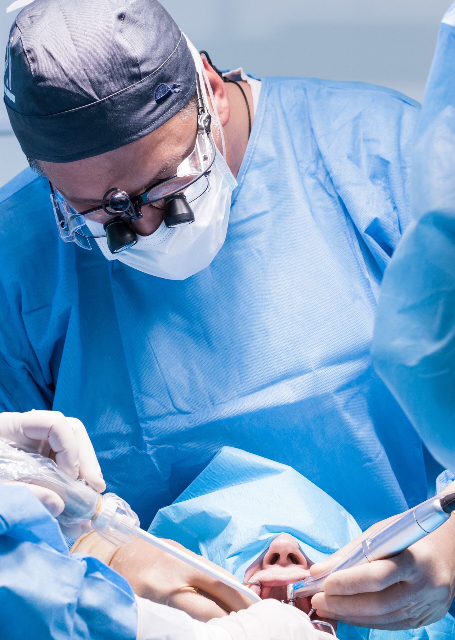 A male dentist in uniform perform dental implantation operation on a patient at dentistry office.