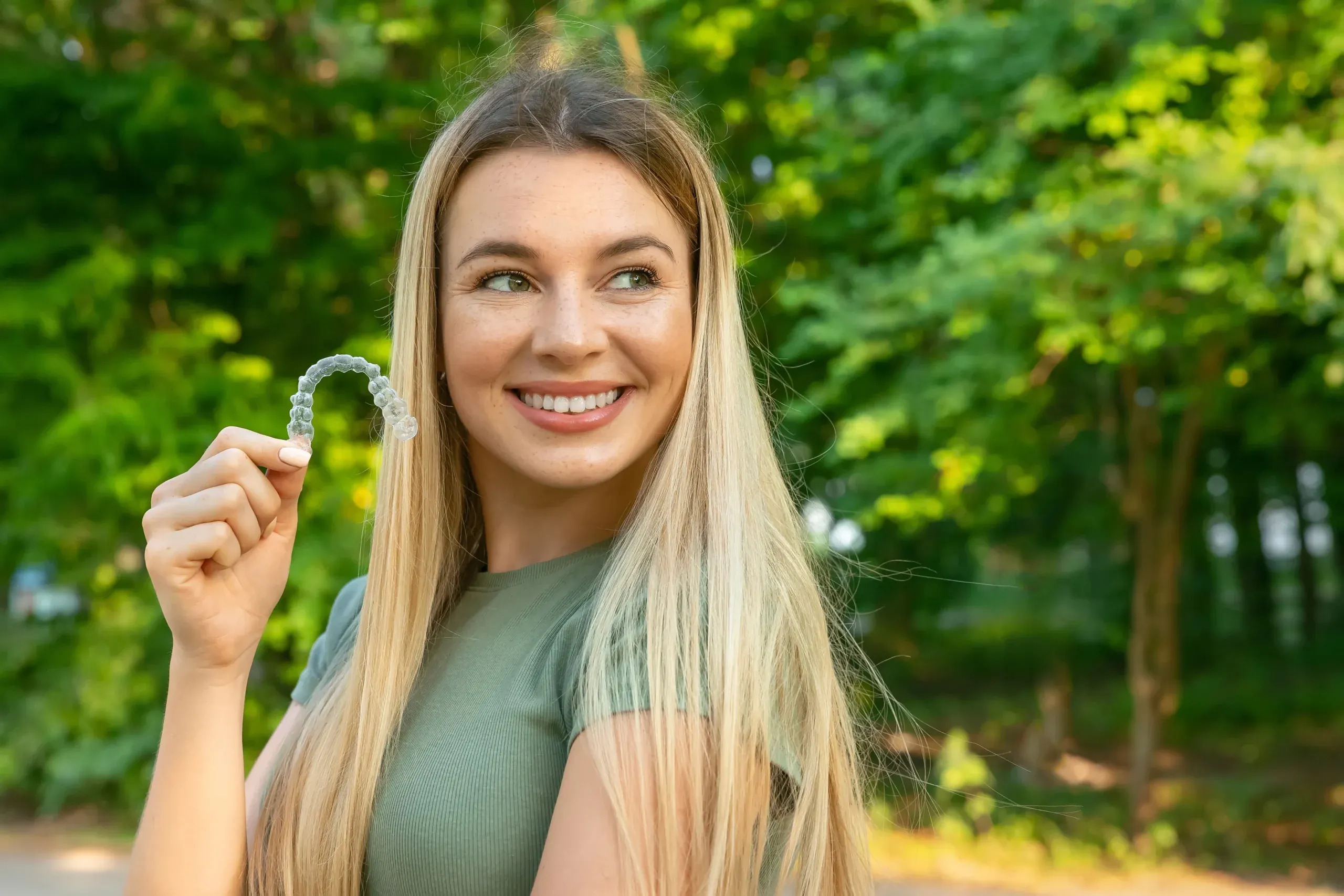Adult smiling while holding a clear Invisalign aligner
